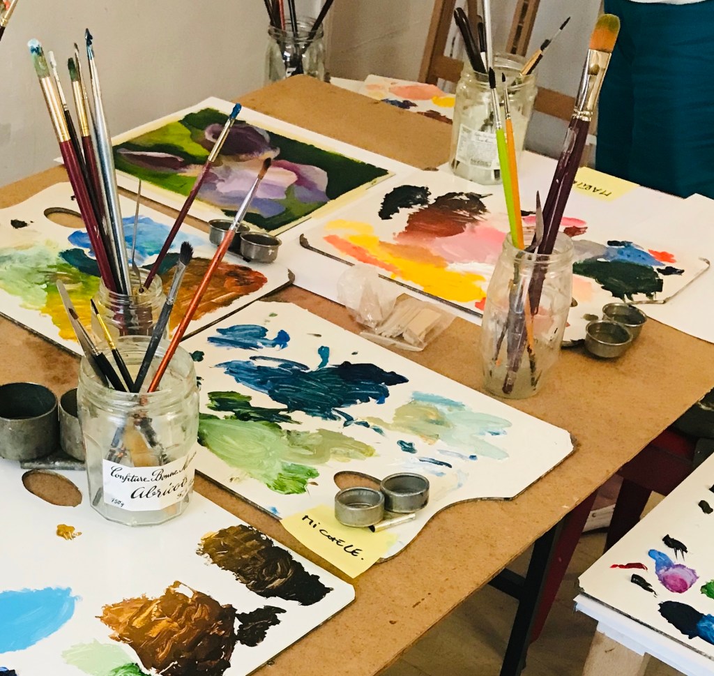 Atelier en cours : palettes de peinture, pinceaux, palettes et productions des participants.