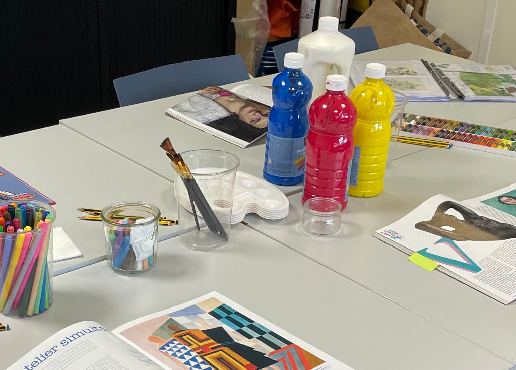 Table installée pour un atelier d'art-thérapie, avec peinture, pinceaux, feutres, pastels et magazines.